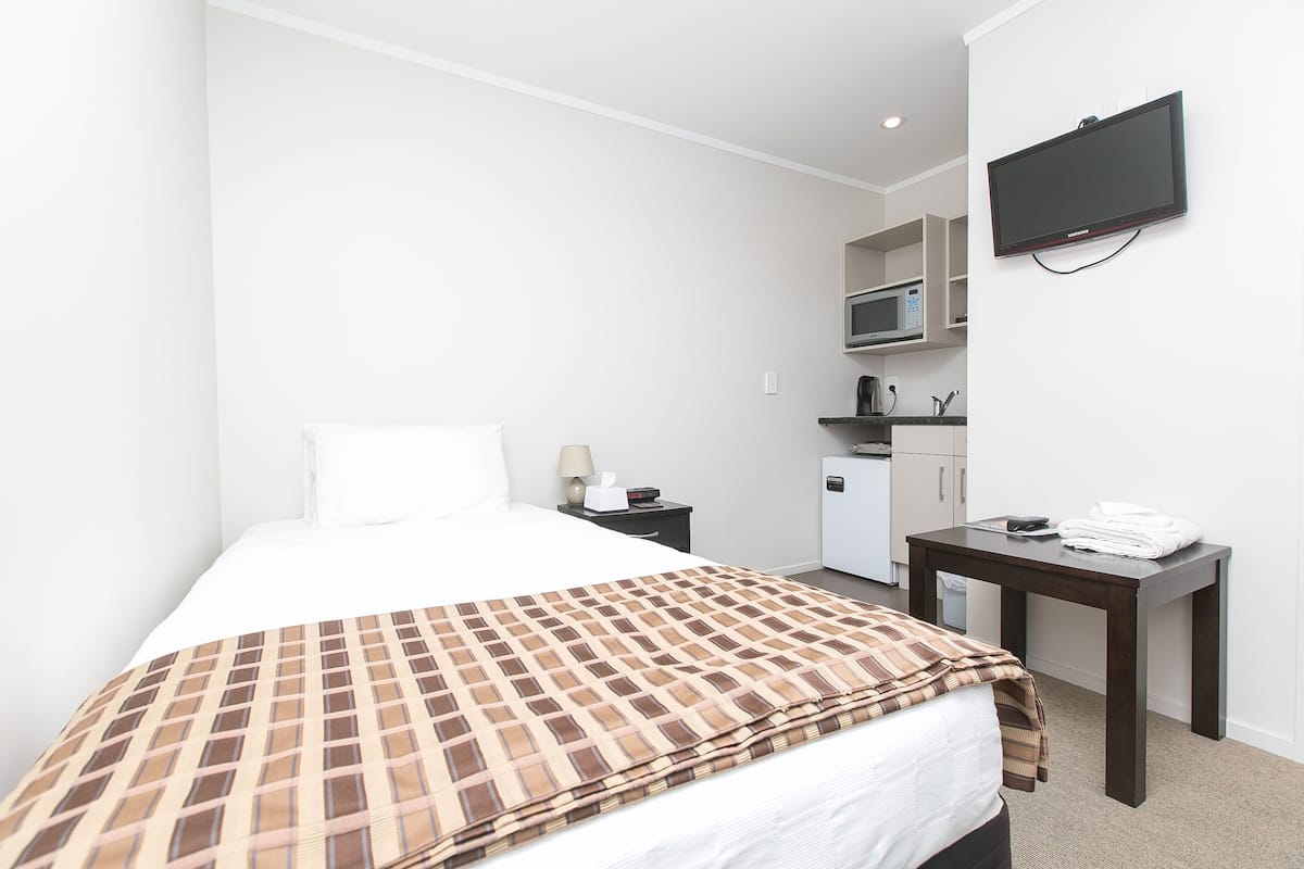 Habitación de hotel con cama, escritorio, televisor de pantalla plana, microondas y kitchenette.