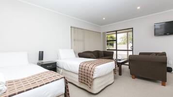 A hotel room with two beds, a sofa, a TV, and a window with blinds.