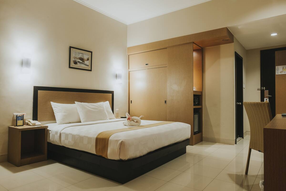 A hotel room with a large bed, a nightstand, a chair, and a wooden wardrobe.