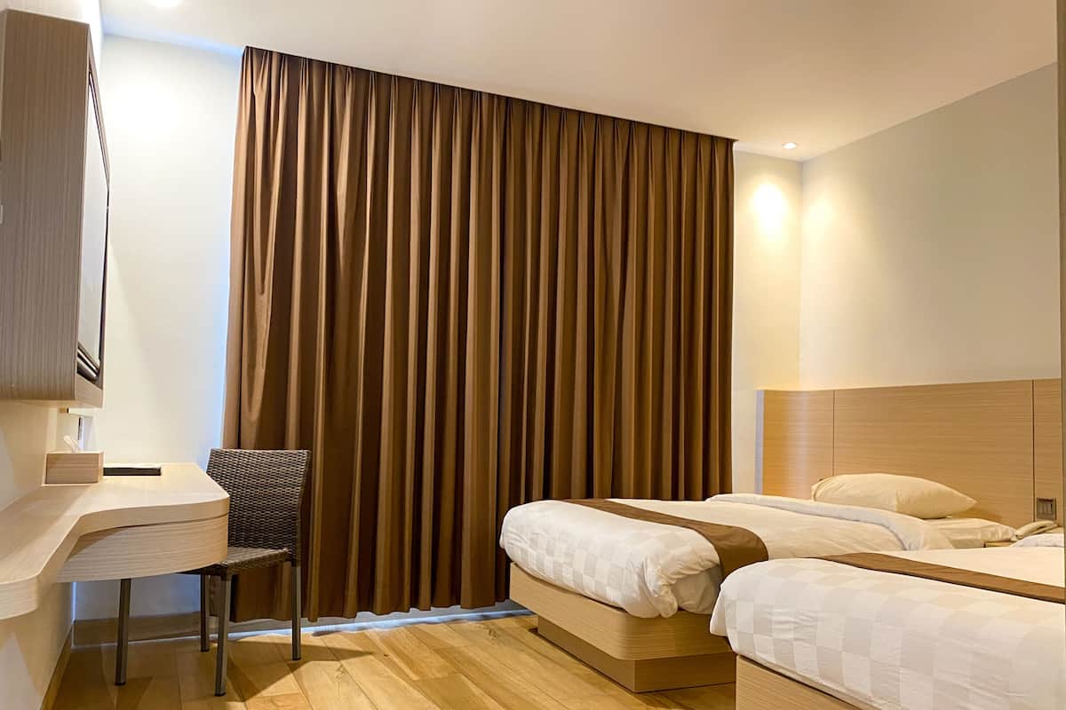 A hotel room with a wooden desk, two beds, a chair, and a large curtain.