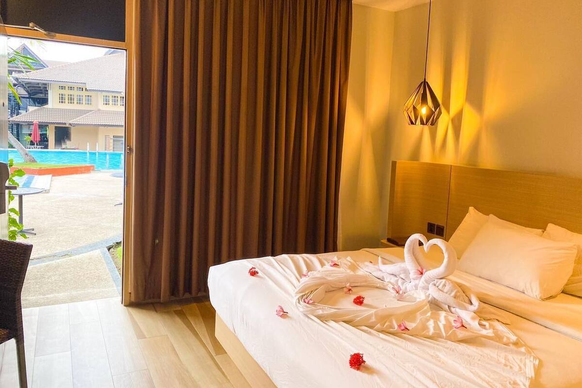 A hotel room with a bed, a view of a swimming pool, and a large window with curtains.