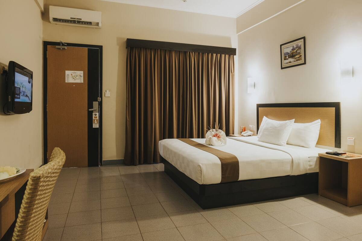 A hotel room with a bed, a desk, a chair, a television, and a window with curtains.