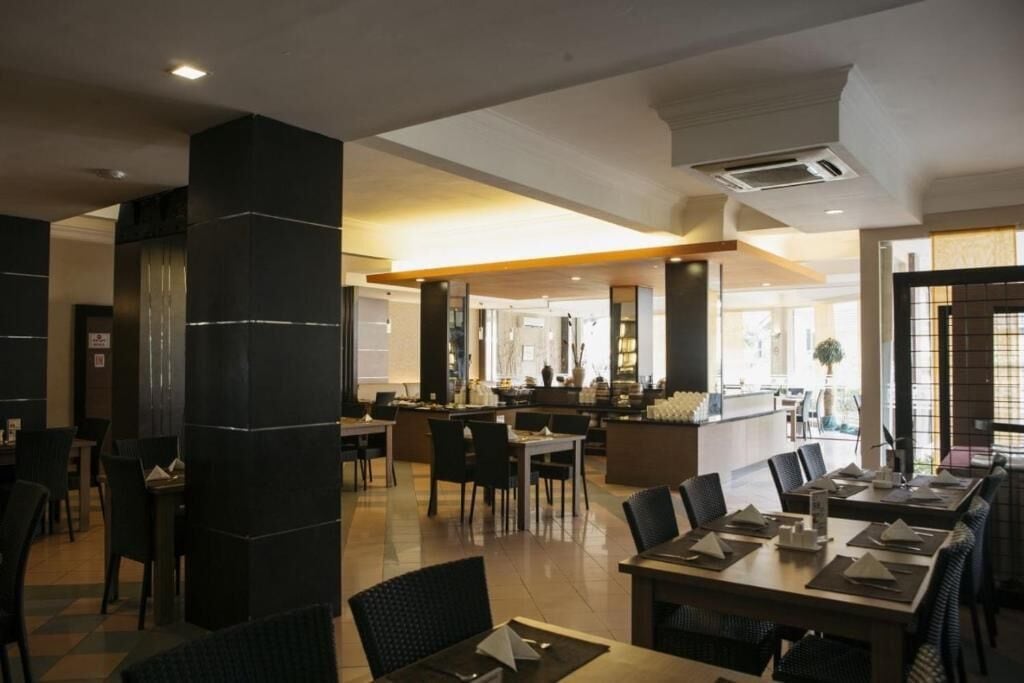 A modern restaurant with high ceilings, black columns, and a mix of seating arrangements including tables and booths.