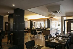 A modern restaurant with high ceilings, black columns, and a mix of seating arrangements including tables and booths.