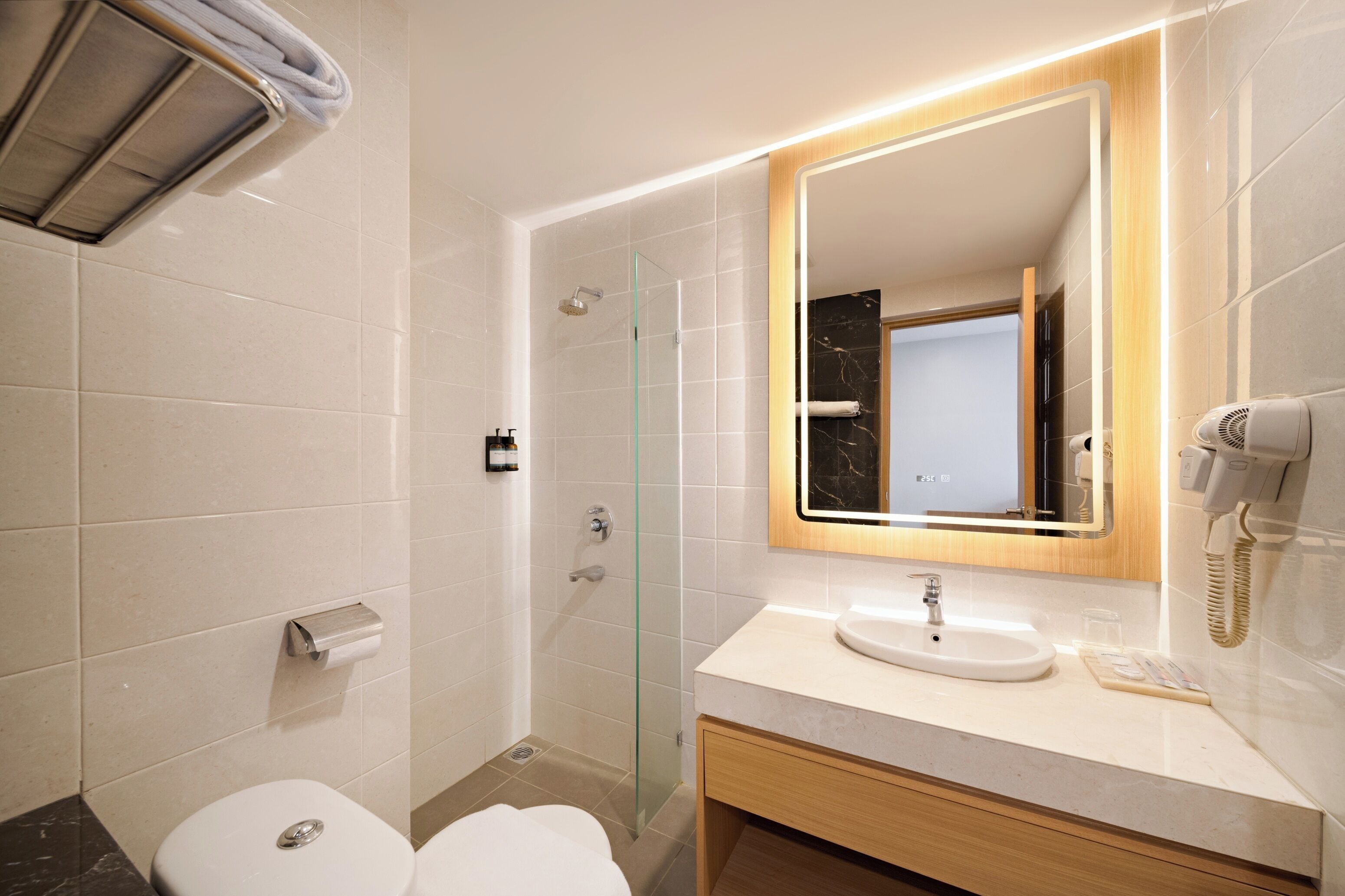 Une salle de bain moderne avec une douche à parois de verre, un lavabo blanc et un miroir doté d’un cadre éclairé.