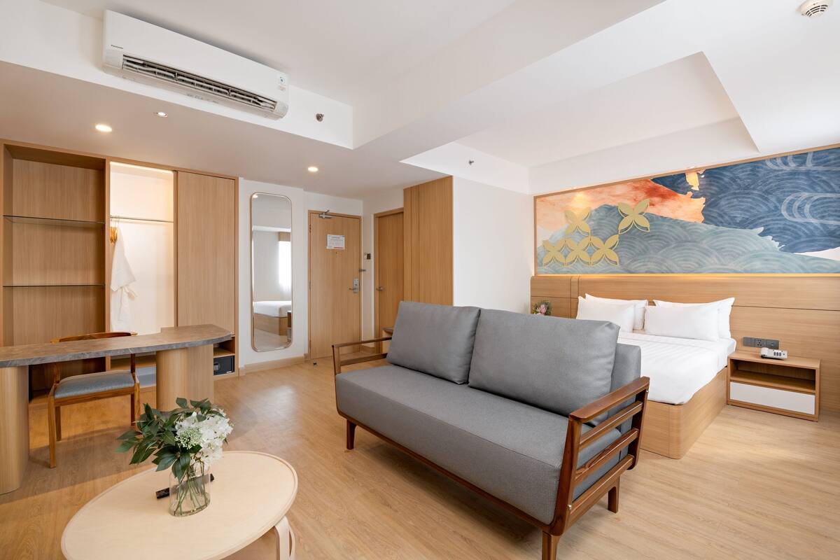 A modern hotel room with a sofa, a bed, a desk, and a dining area.