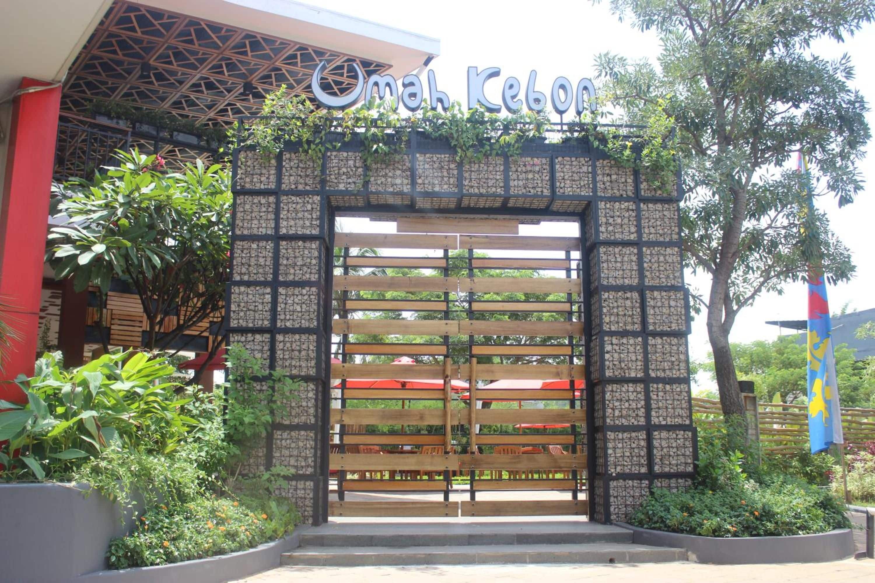 A hotel entrance with a sign above the gate, a wooden gate, and surrounding greenery.