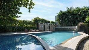 A swimming pool with a tiled edge, surrounded by lush greenery and a small building with a tiled roof. - Metland Hotel Bekasi (Cikarang)