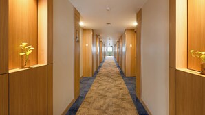 A hotel hallway with wooden paneling, a blue carpet, and potted plants on the walls. - Metland Hotel Bekasi (Cikarang)