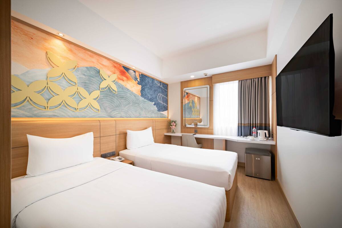 A hotel room with two beds, a desk, a small kitchenette, and a large wall mural.