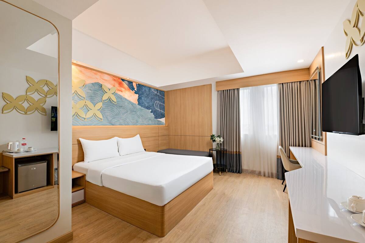 A hotel room with a bed, desk, TV, and artwork on the wall.
