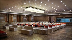 Un salón de conferencias amplio con filas de sillas, un escenario y una pantalla grande.