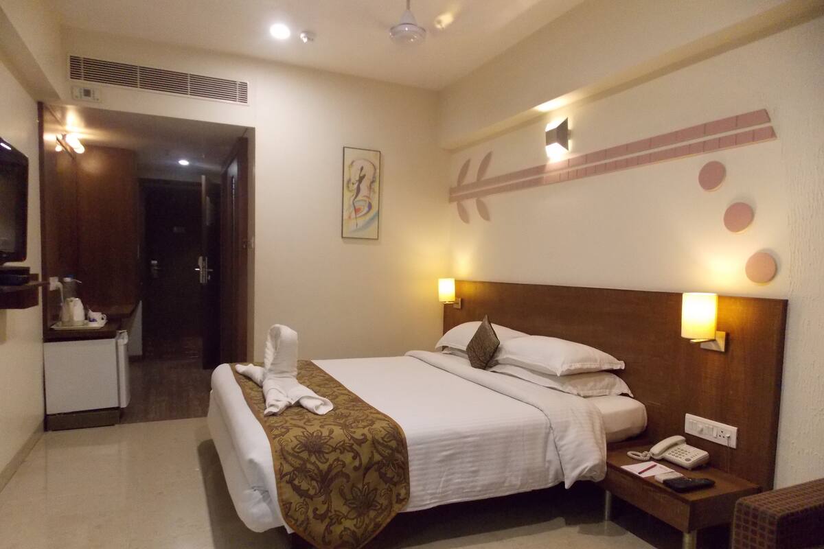 A hotel room with a bed, bedside table with a phone, and a wall-mounted light fixture.