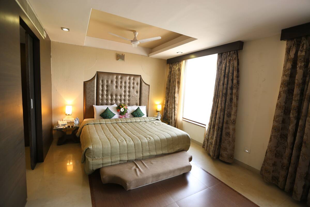A hotel room with a large bed, a ceiling fan, a nightstand, and a window with curtains.