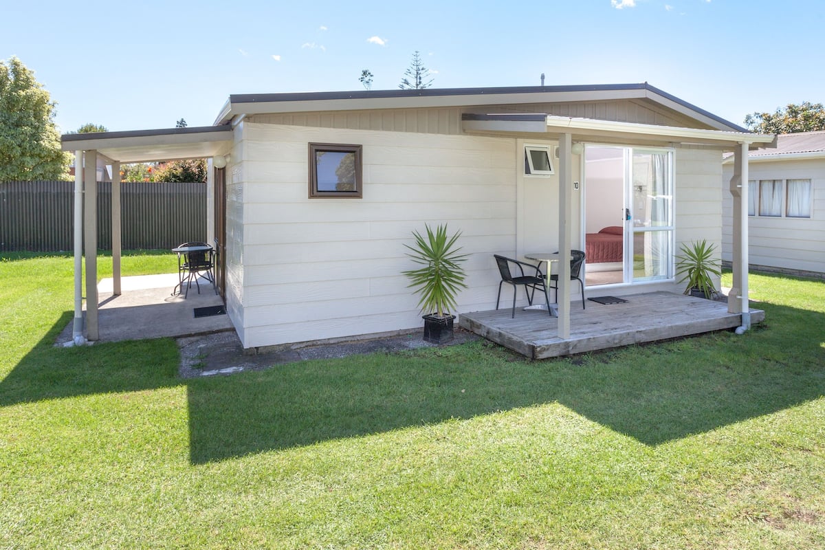 Une maison de plain-pied avec un patio couvert, une petite table et des chaises, et une plante en pot.