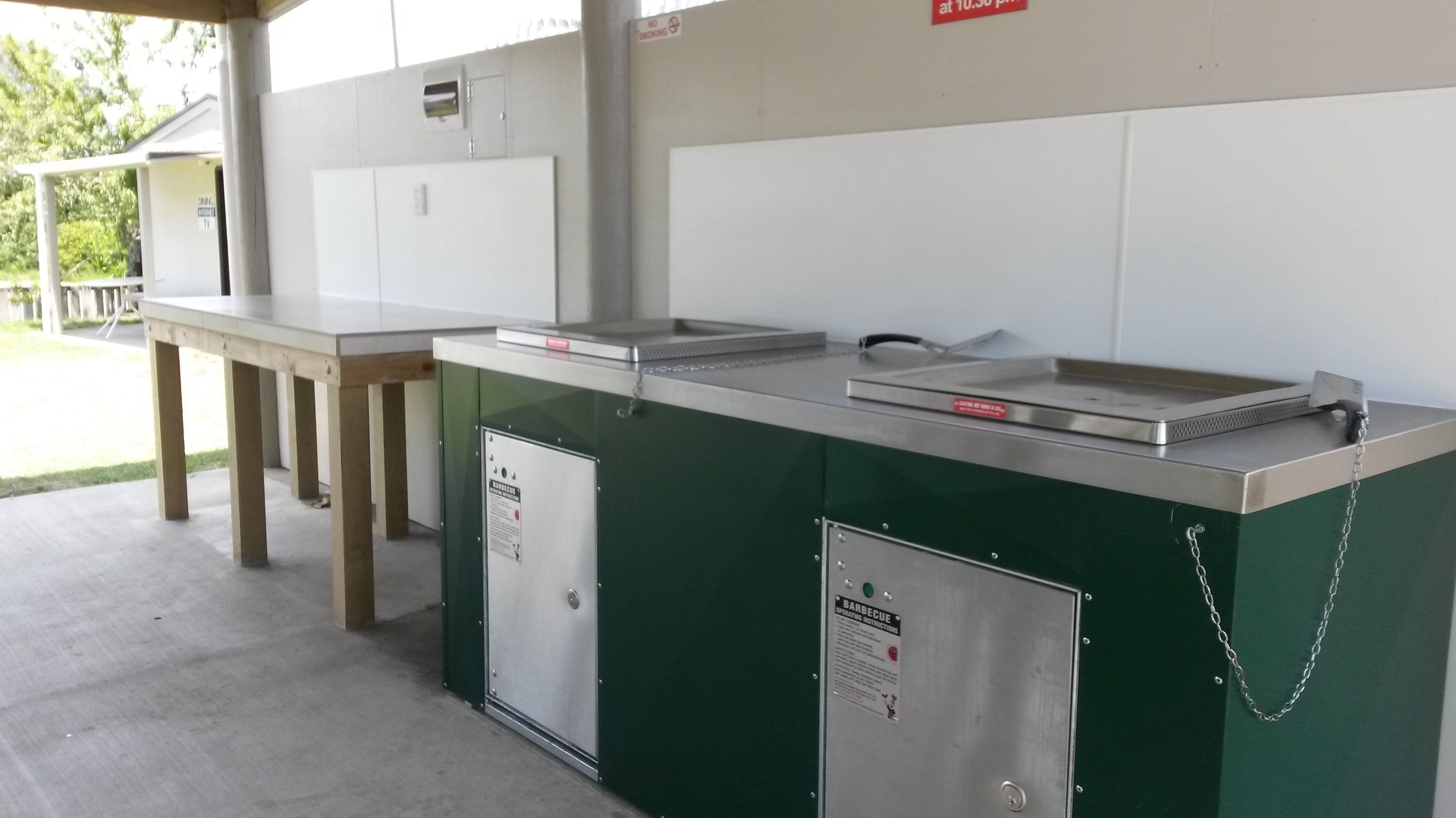 A barbecuing station with a grill, a table, and a cabinet.