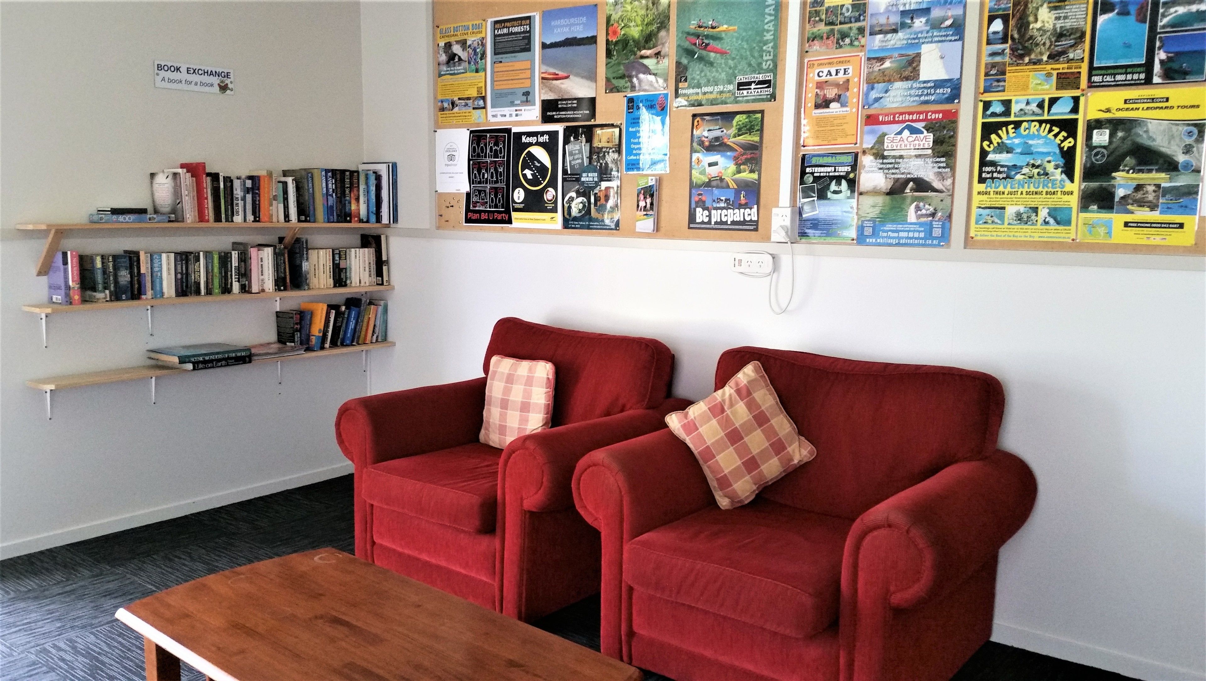 Een kamer met een rode zithoek, een houten bijzettafeltje en een boekenplank vol boeken.
