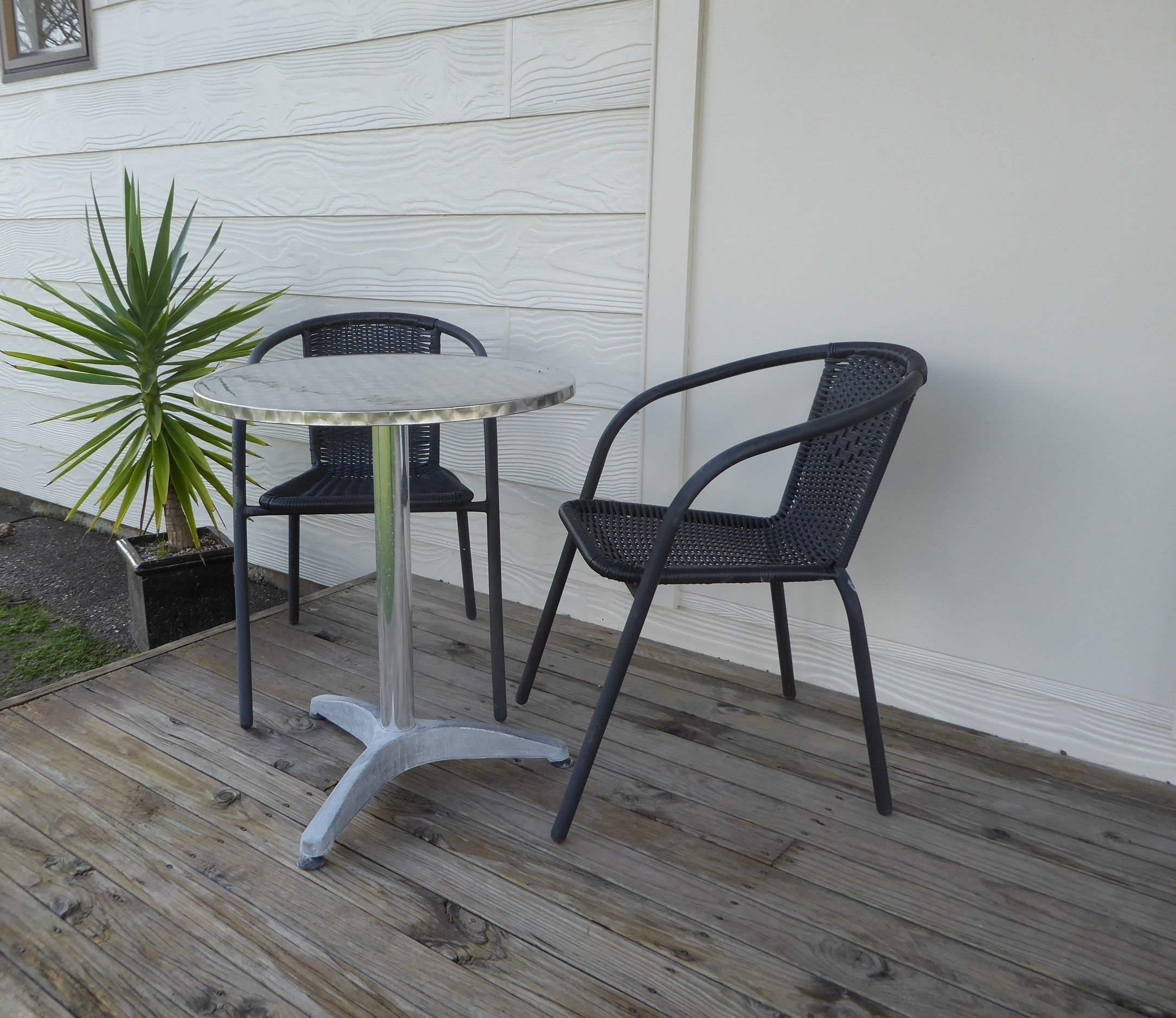 Un pequeño patio al aire libre con una mesa redonda y dos sillas, una planta en maceta y una terraza de madera.