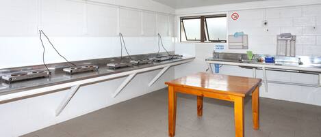 Una cocina con paredes de azulejos blancos, encimeras de acero inoxidable y una mesa de madera.