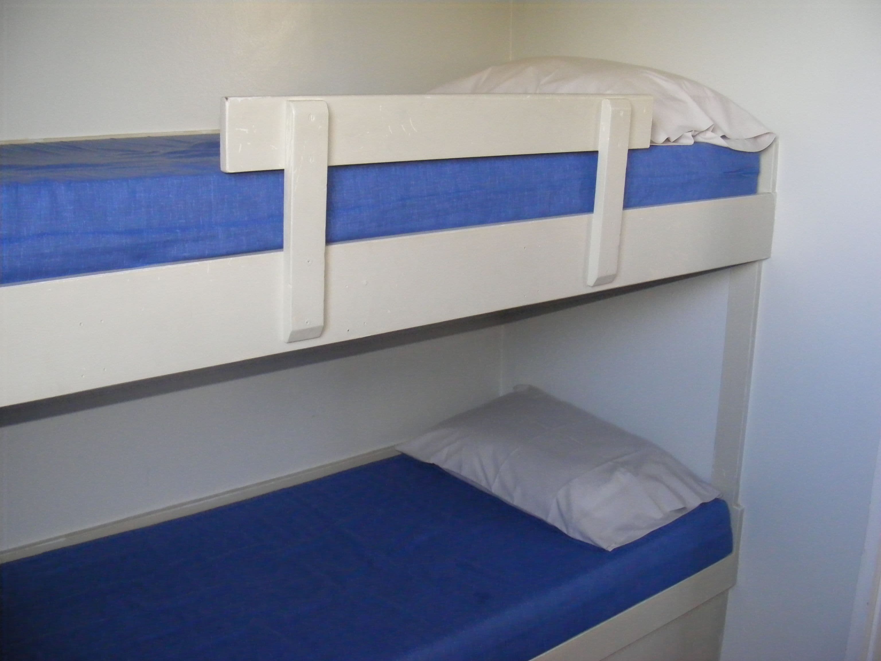 A bunk bed with a blue mattress and white bedding.