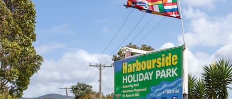 A sign for Harbourside Holiday Park advertising amenities like a swimming pool, adventure playground, TV room, BBQ, and wireless internet.