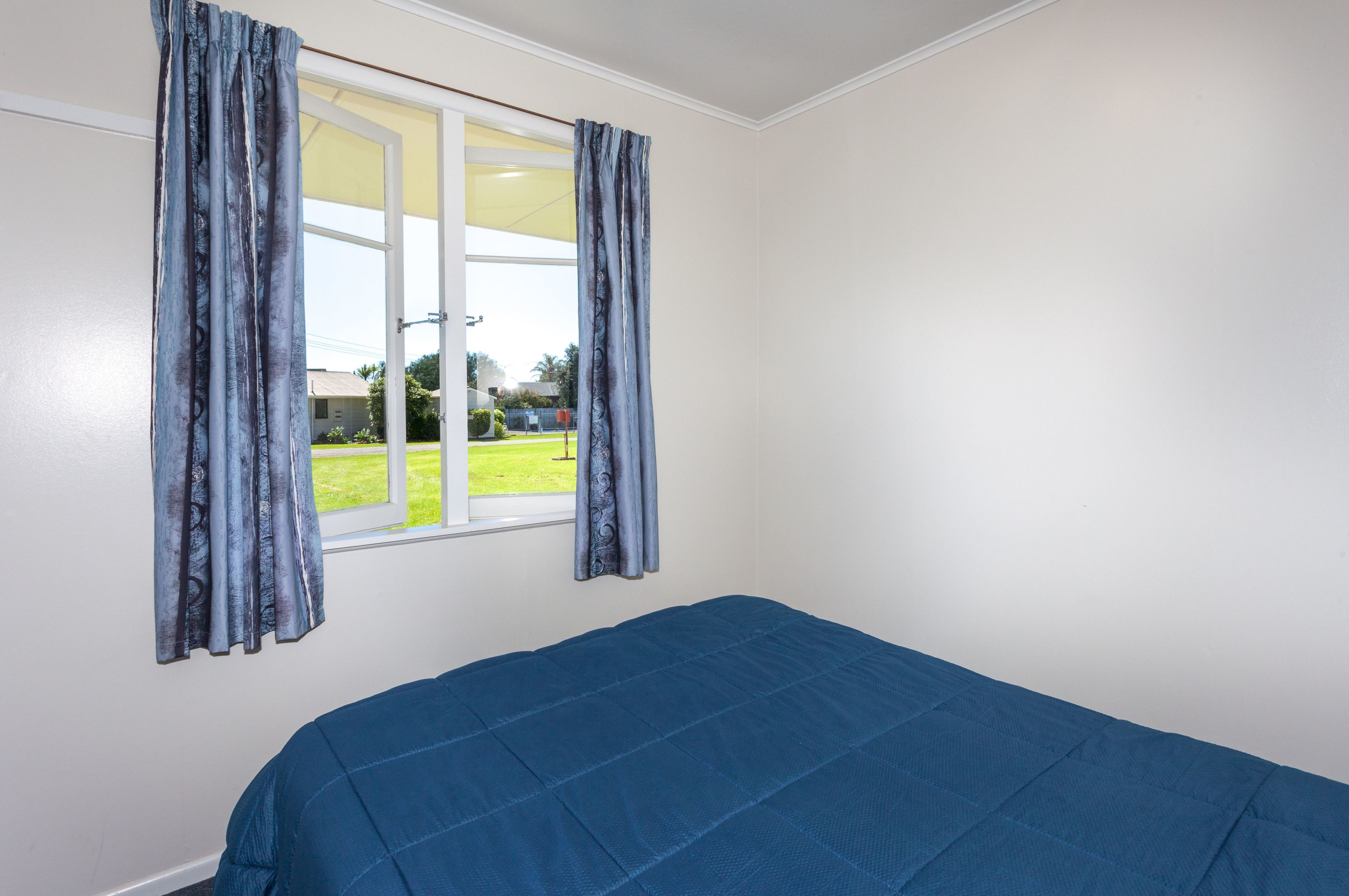 Una habitación con una cama, un ventanal con cortinas y vistas a un césped verde.