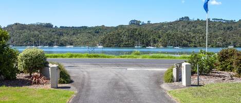 A paved road leading to a body of water with boats, surrounded by greenery and a flagpole.