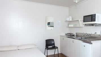 A compact hotel room with a bed, a small kitchenette, a microwave, a sink, and a chair.