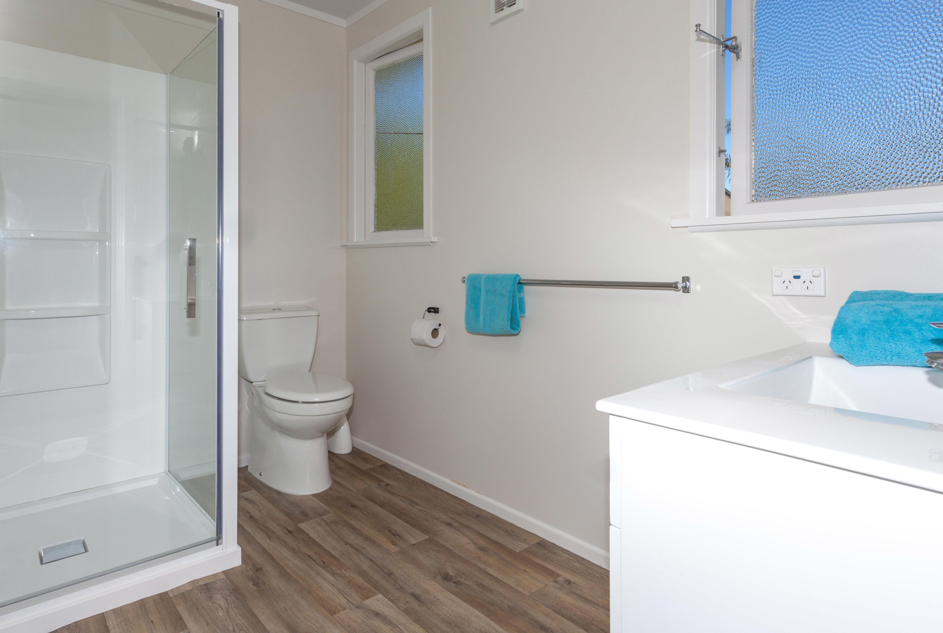 Een badkamer met een glazen douchecabine, toilet, raam en een wastafel met een handdoek.