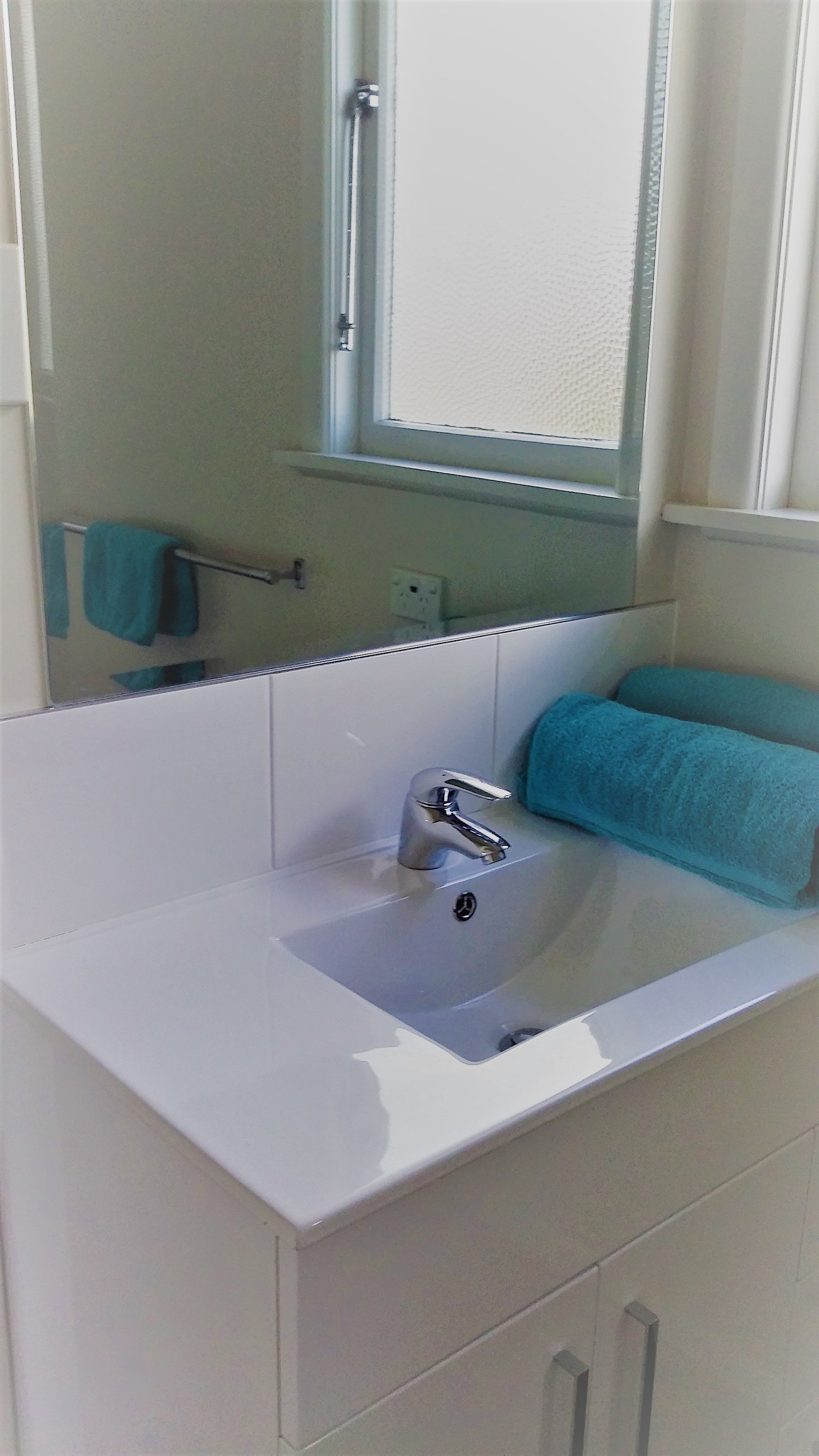 Une salle de bain avec un lavabo blanc, un miroir et une fenêtre.