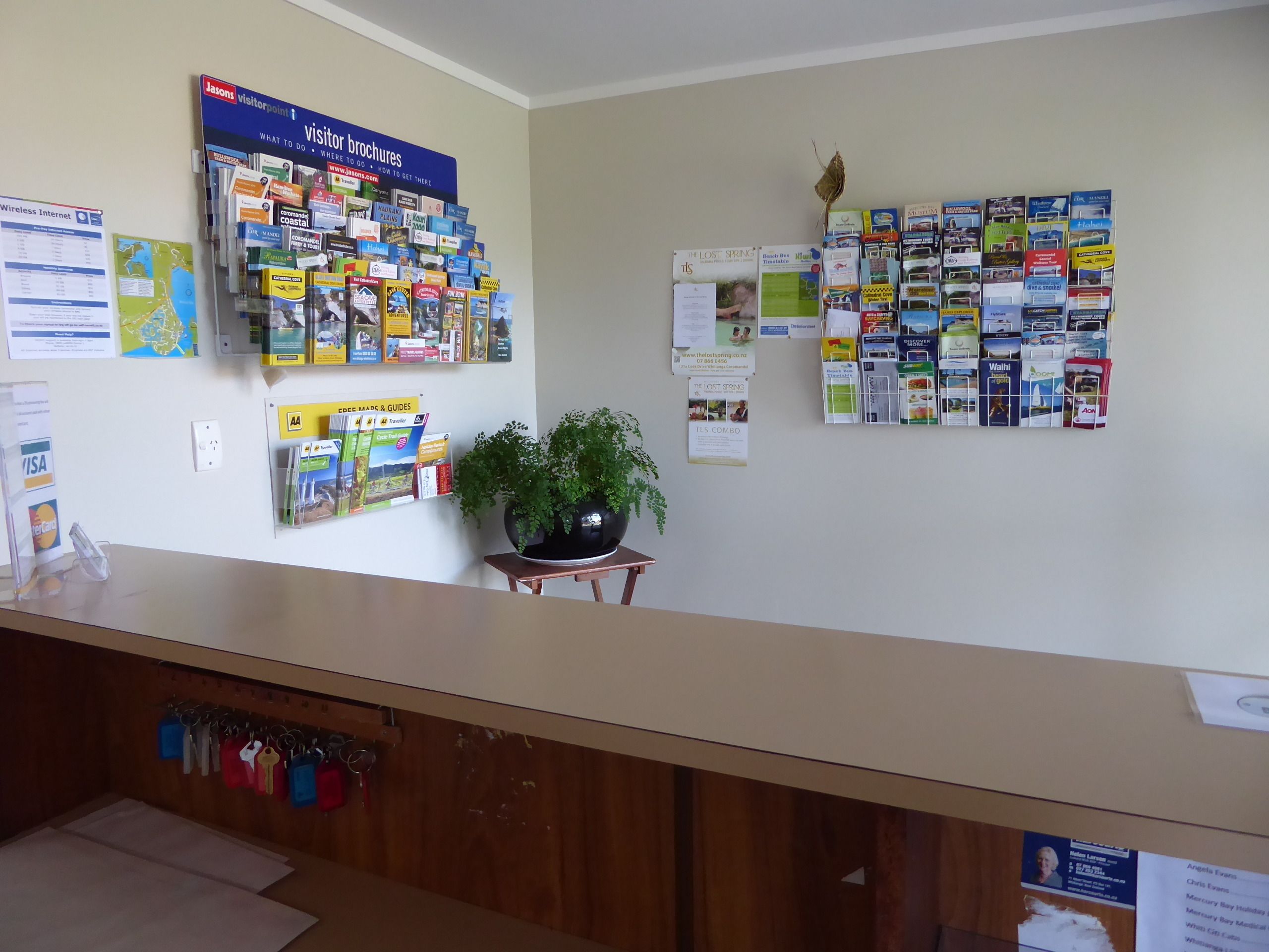 A reception area with a wall display of brochures, a plant, and a sign for visitor information.
