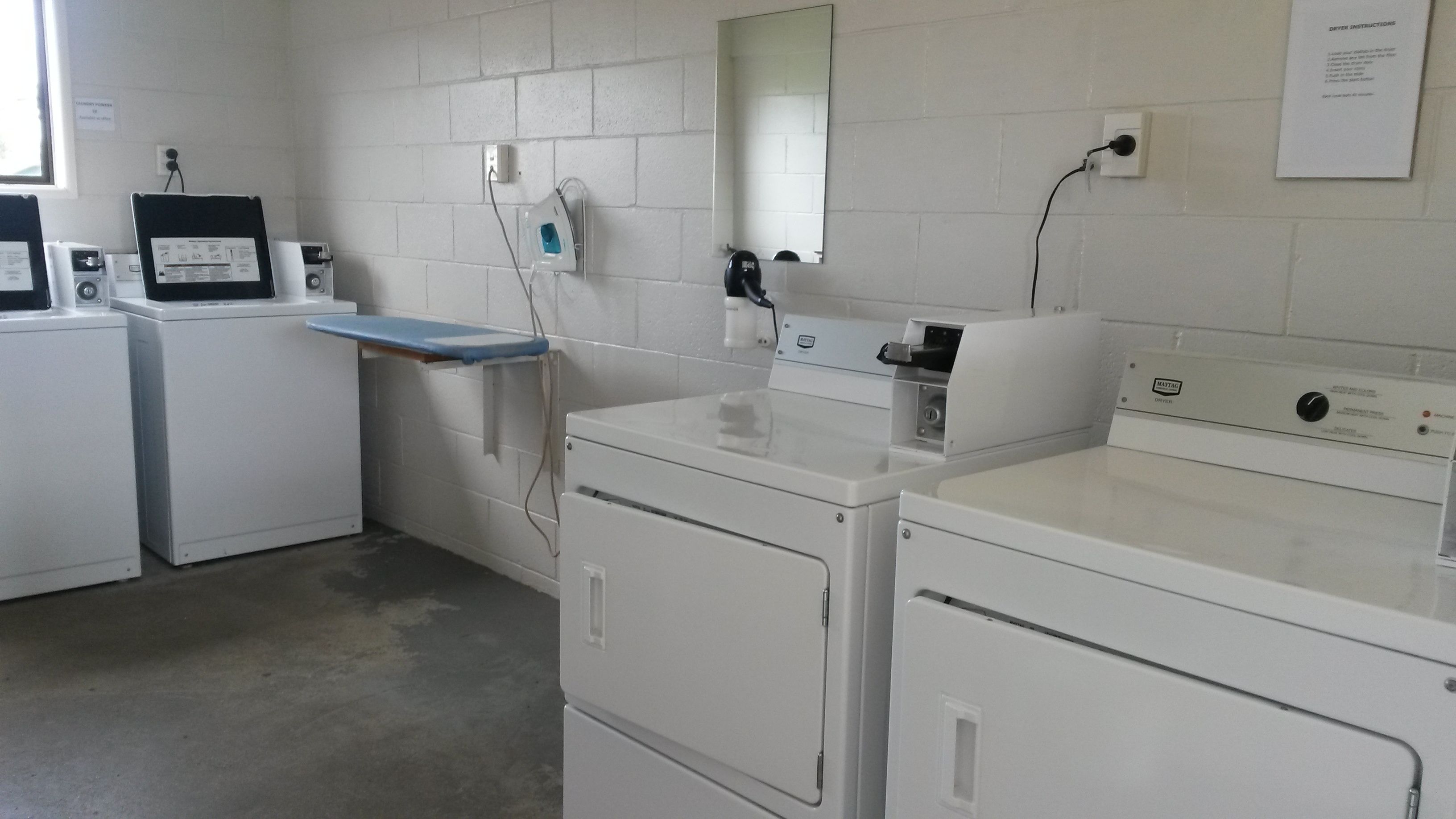 A laundry room with stacked washers and dryers, a blue shelf, and a mirror on the wall.