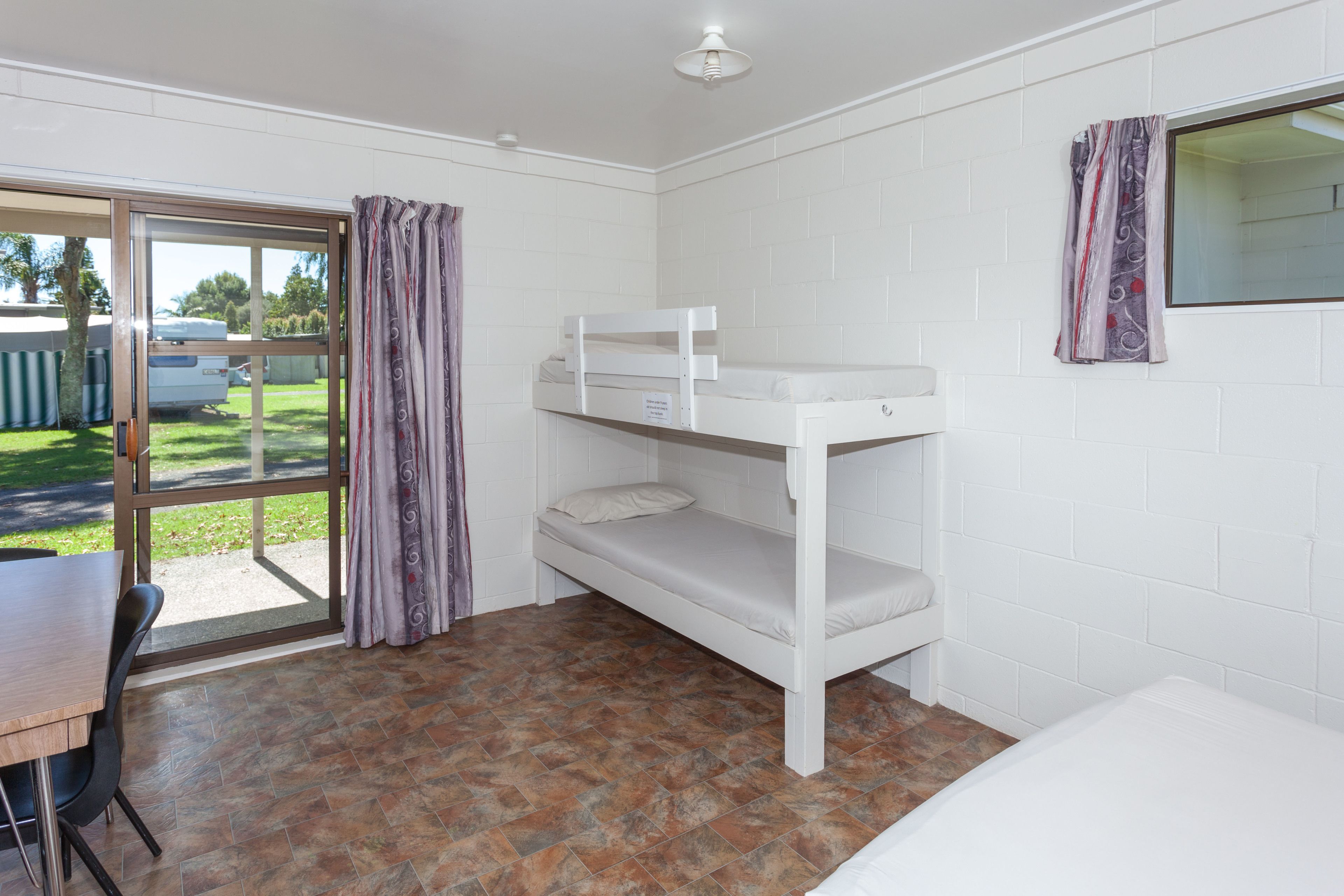Ein Zimmer mit einem Etagenbett, einem Tisch und einem Fenster mit Vorhängen.