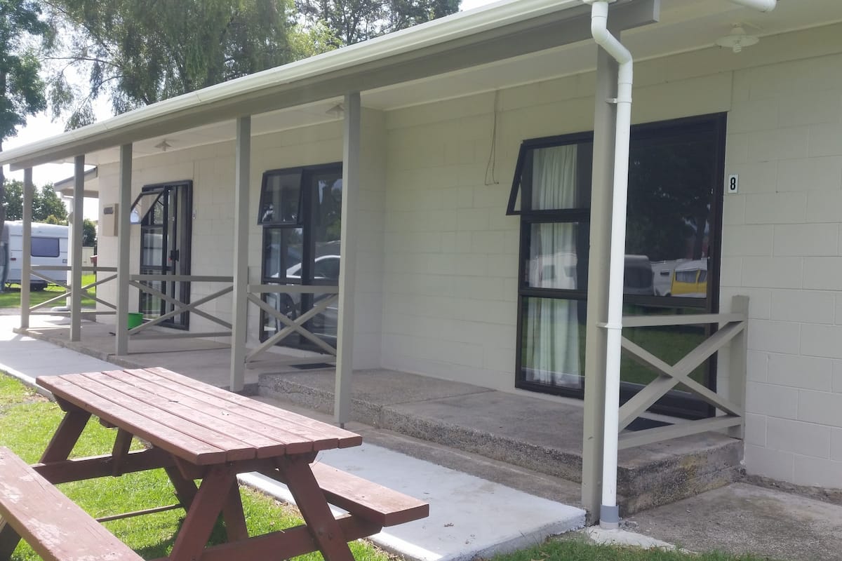 Une rangée de chalets de plain-pied, chacun doté d’un porche individuel et d’une table de pique-nique située au premier plan.