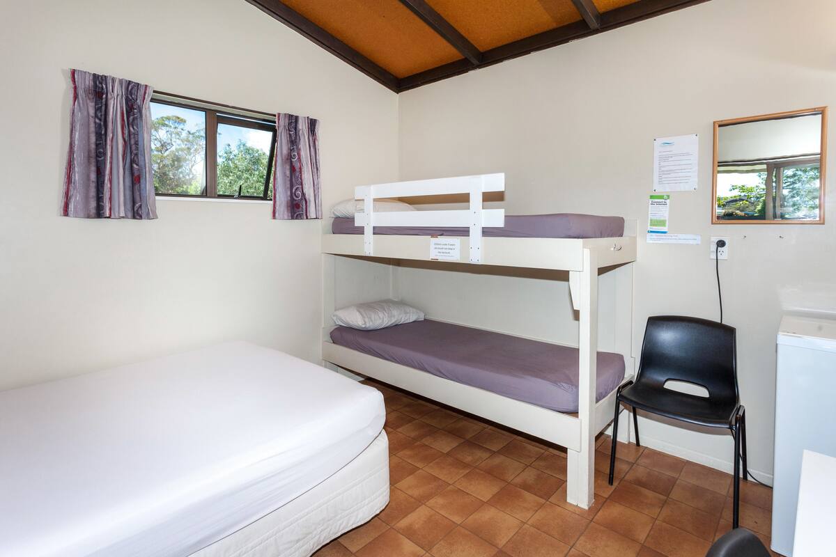 Une chambre avec un lit superposé, un matelas, une chaise, un bureau et une fenêtre avec des rideaux.