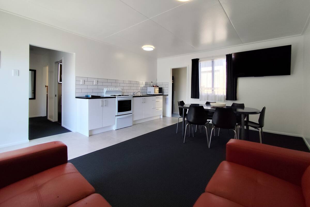 A modern kitchen with white cabinets, a stove, and a dining area with black chairs and a red couch.