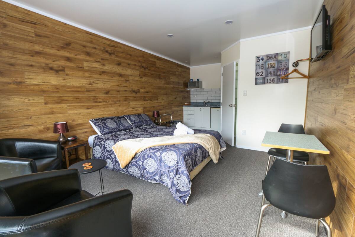 A bedroom with a bed, a desk, a chair, a small table, and a wardrobe.