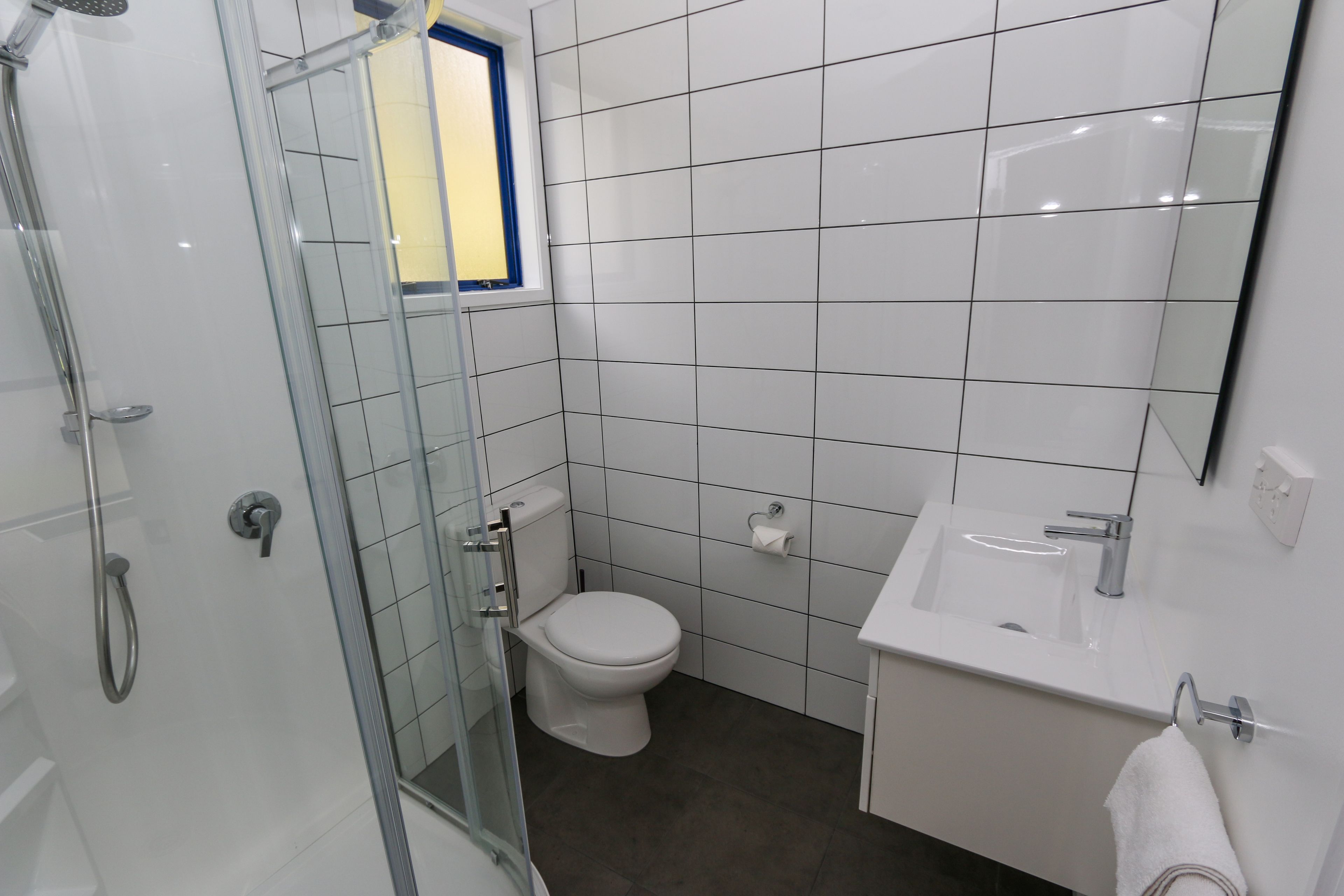 Un baño moderno con cabina de ducha de vidrio, inodoro blanco y lavamanos con espejo.
