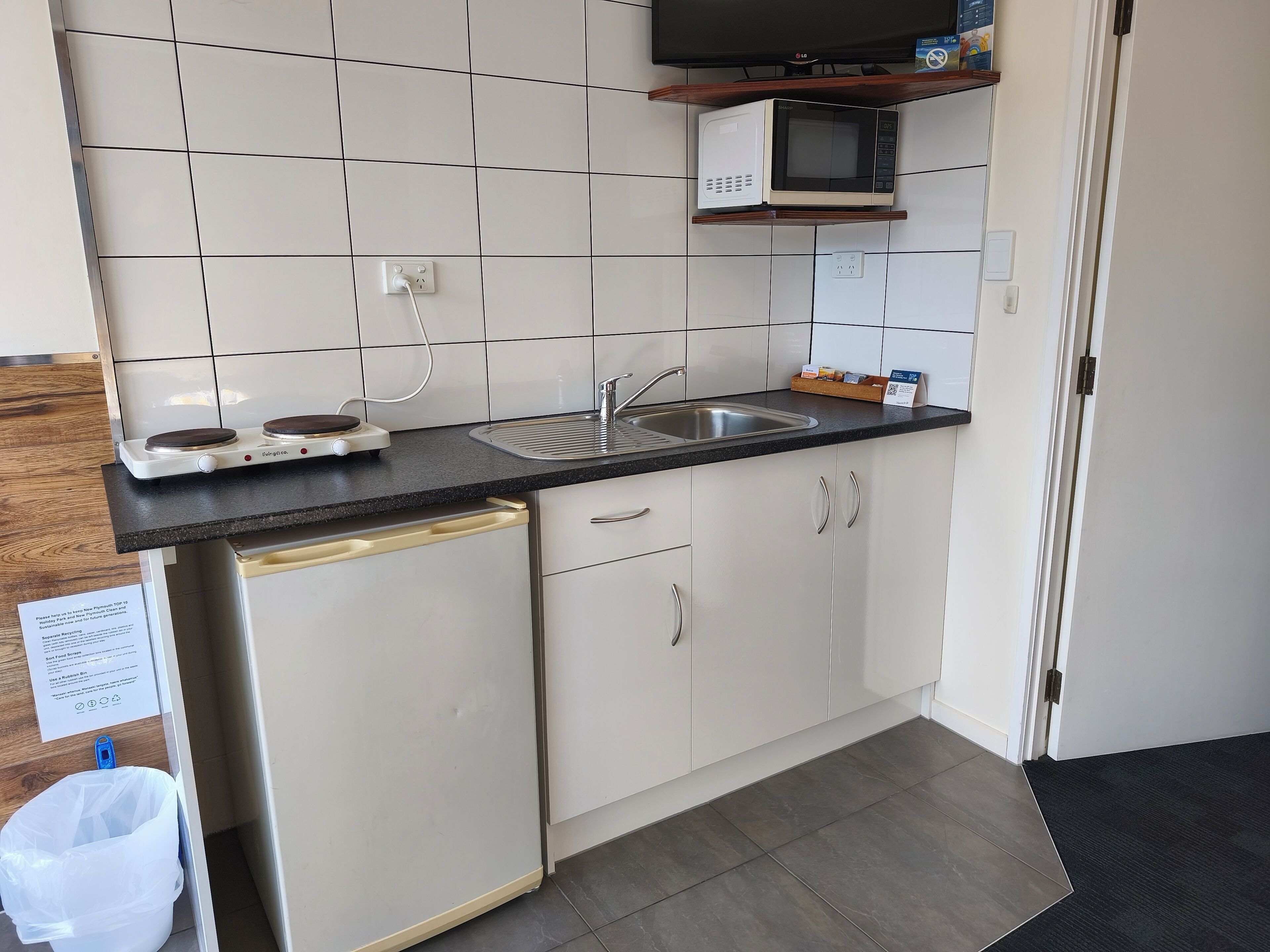 A kitchen with white cabinets, a black countertop, a microwave, a sink, and a dishwashing unit.