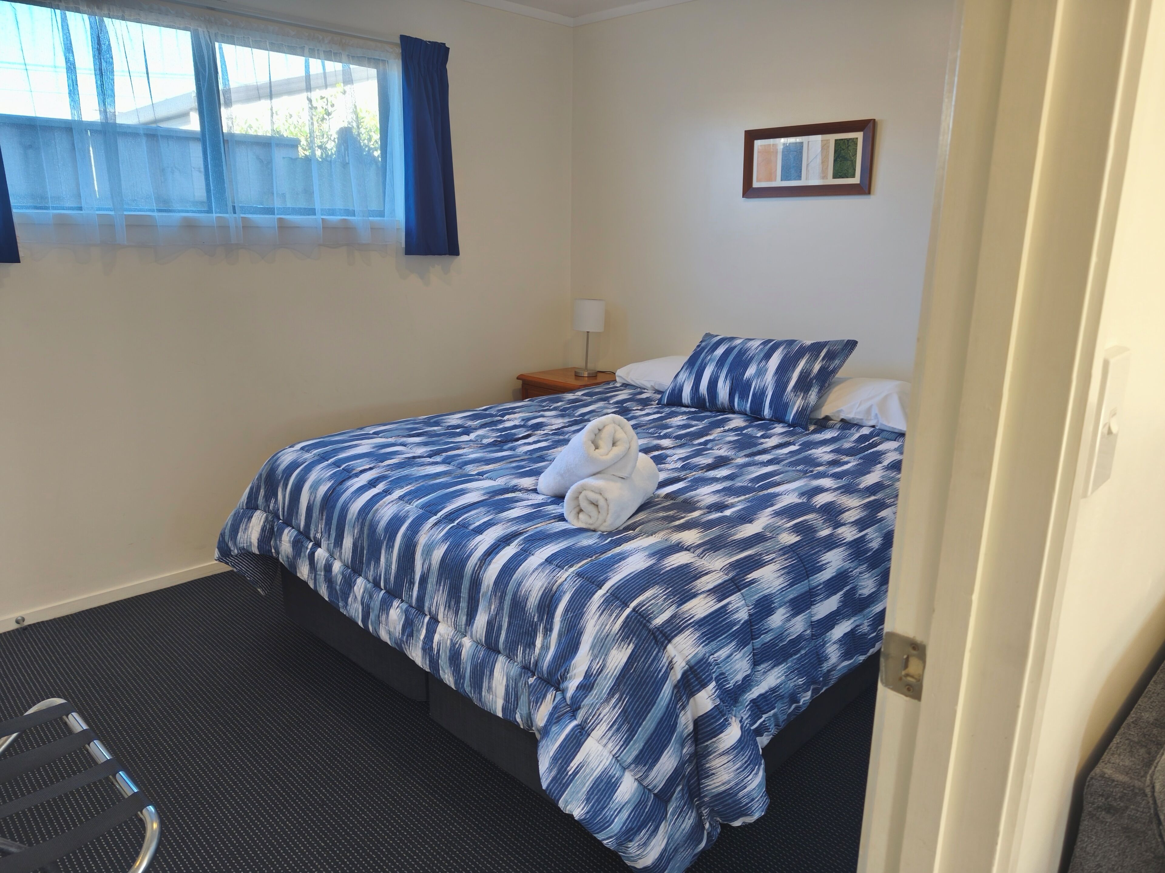 A hotel room with a bed, a nightstand, a lamp, and a window with curtains.