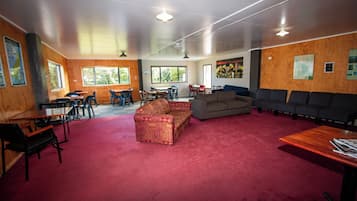 A spacious room with a red carpet, wooden walls, a sofa, a couch, and a dining area with chairs and tables.