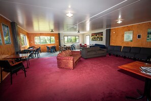 A spacious room with a red carpet, wooden walls, a sofa, a couch, and a dining area with chairs and tables. - New Plymouth Top 10 Holiday Park (New Plymouth)