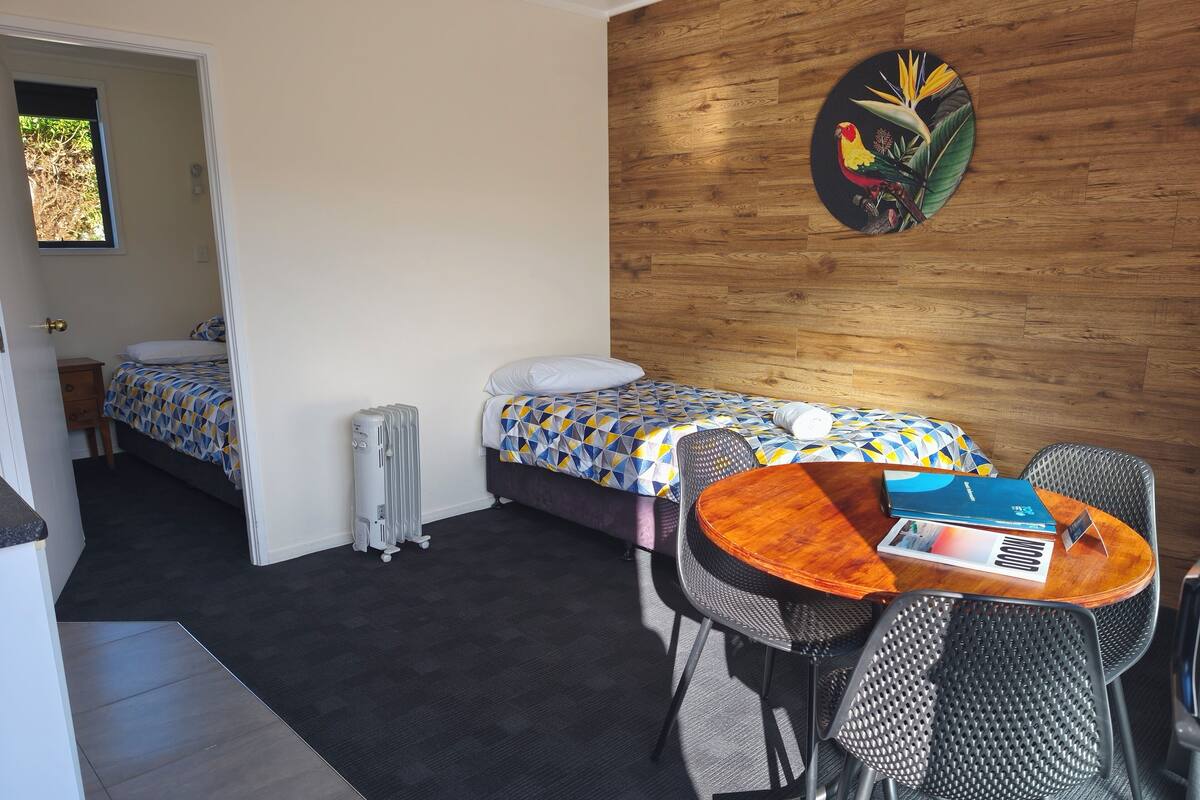 A room with a bed, a table with chairs, a radiator, and a wall-mounted artwork.