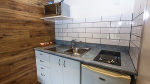 A kitchen with a wooden wall, white cabinets, a sink, a stove, and a microwave. - New Plymouth Top 10 Holiday Park (New Plymouth)