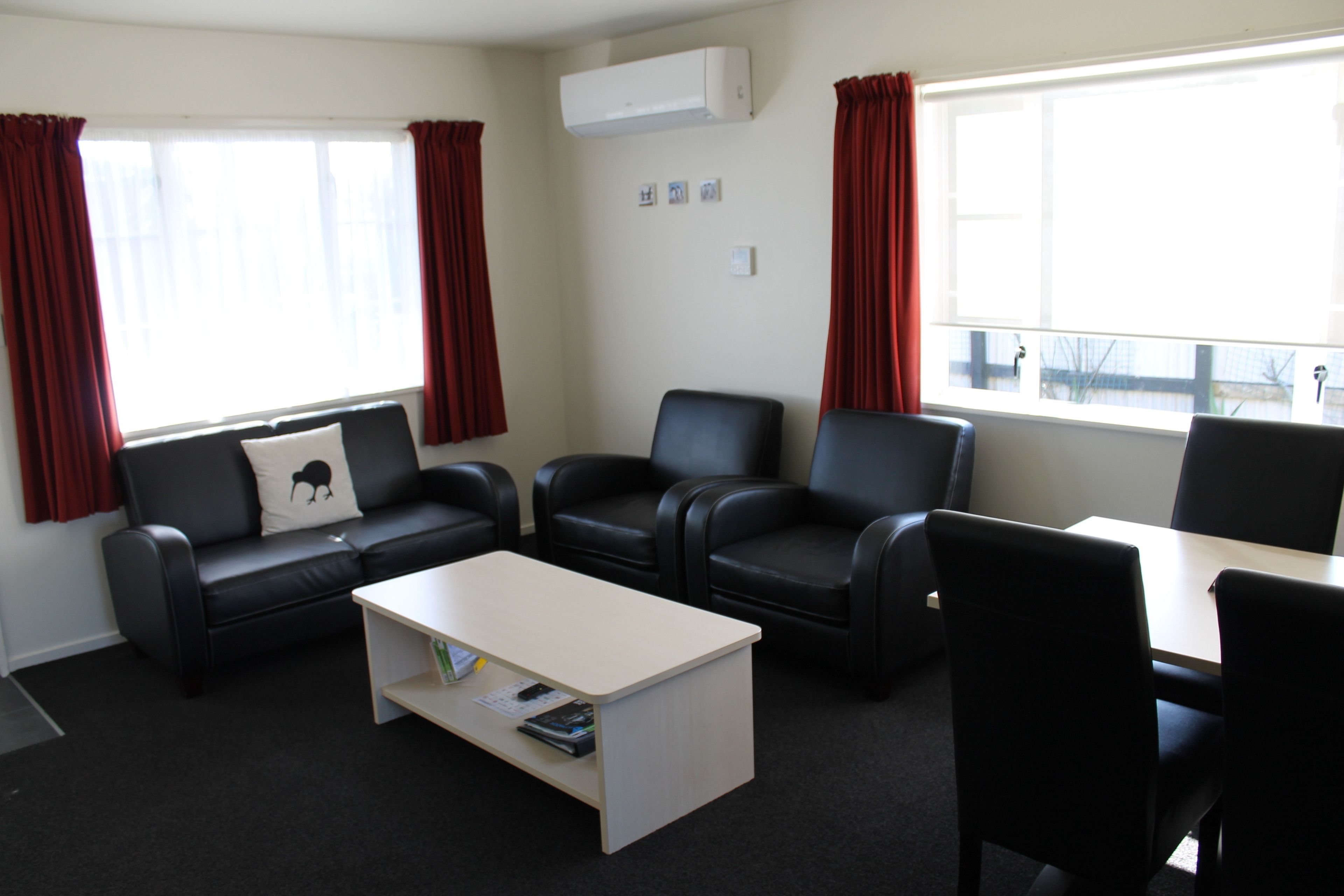 Ein Zimmer mit einer schwarzen Ledersofa, zwei schwarzen Sesseln, einem weißen Couchtisch und einem kleinen Tisch mit Stühlen.