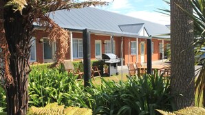 A building with a covered patio area, a barbecue grill, and outdoor seating. - Alpine Rose Greymouth Motel (Greymouth)