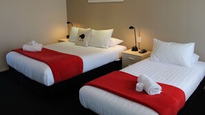 Two adjacent hotel beds with white linens and red blankets, each with a pillow and a rolled towel. - Alpine Rose Greymouth Motel (Greymouth)