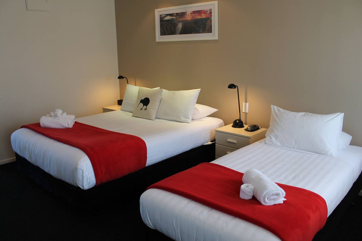 Two adjacent hotel beds with white linens and red blankets, each with a pillow and a rolled towel.