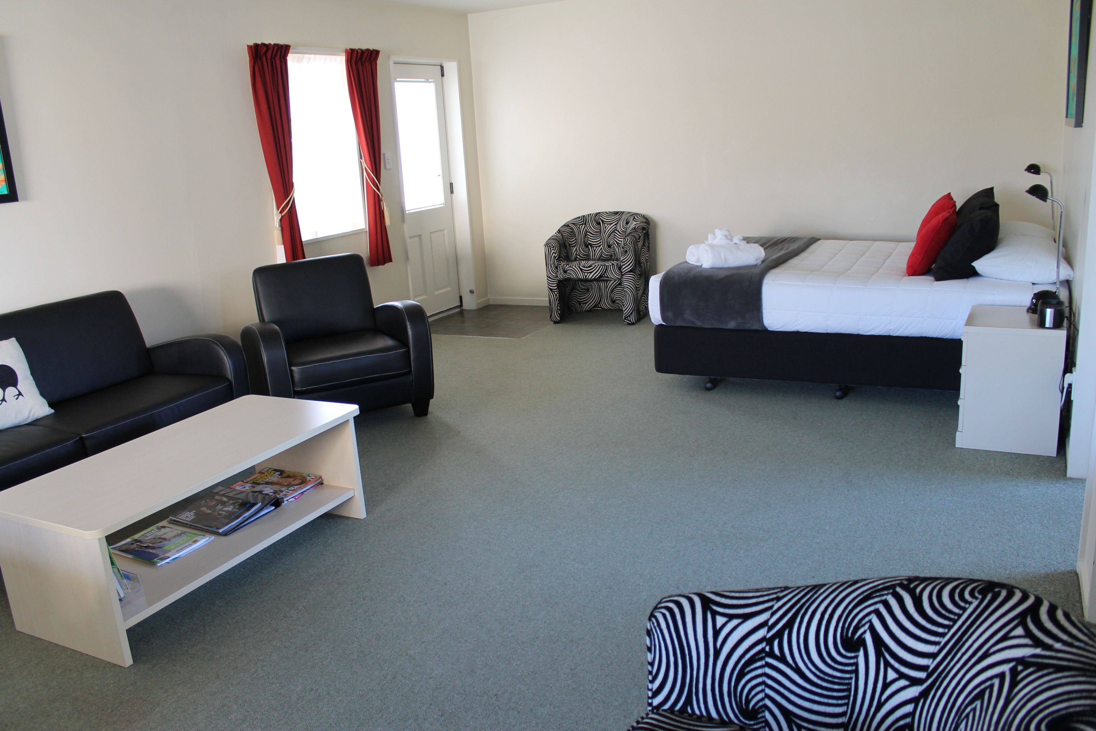 Habitación de hotel con cama, sofá, sillón, mesa de centro y pequeño escritorio.