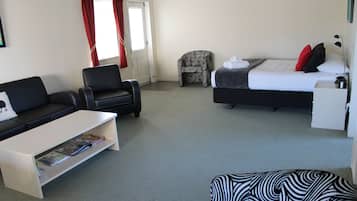 Habitación de hotel con cama, sofá, sillón, mesa de centro y pequeño escritorio.